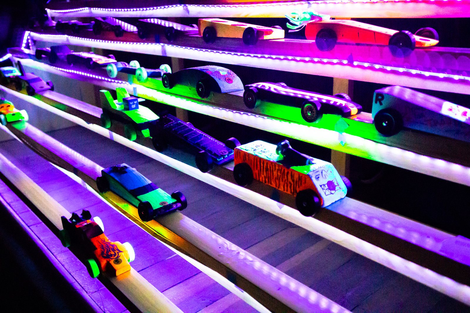 Colorful Pinewood Derby cars lined up on a glowing track